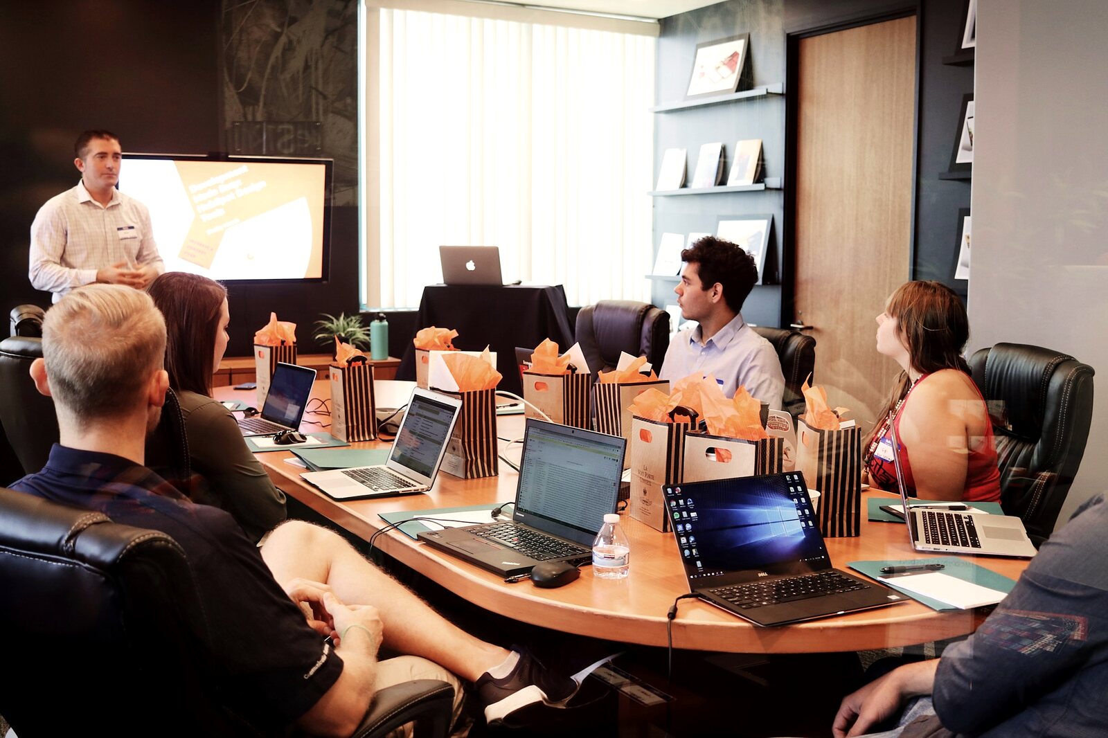 Team at laptops around a table while a colleague presents